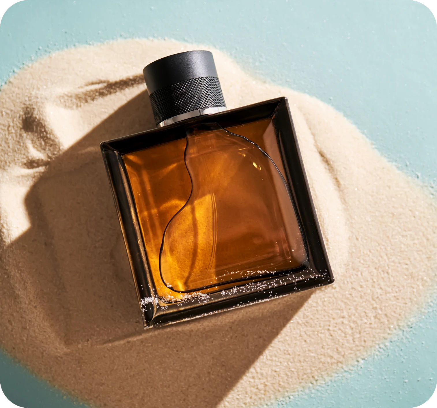 Fragrance bottle displayed on textured sand surface.